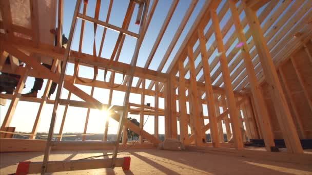 View of builders covering roof with waterproofing layer at unfinished frame house interior with wooden beams of roof and walls with blue sky on background — Stock Footage View Builders Covering Roof Waterproofing Layer Unfinished Frame House Interior Video Clip