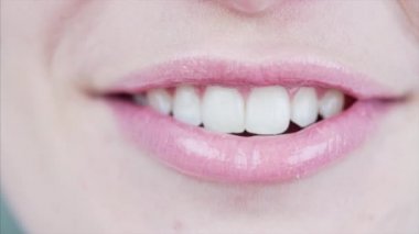 Dudaklarında açık pembe ruj ve güzel beyaz dişlerle konuşan ve gülümseyen kadın ağzının makro görüntüsü.
