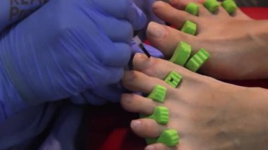 Güzellik salonunda manikür yapan bir kadın. Güzellik uzmanının aplikatörle tırnak cilası sürüşünü yakından görüyor. Usta tırnaklarını cila ile boyadı. Kırmızı çivi takarken çekilmiş detaylar..