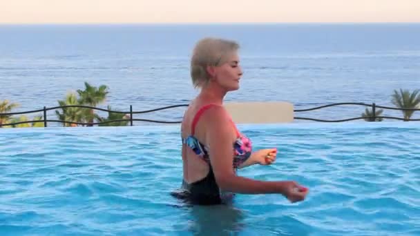 Beautiful woman dancing in the infinity-edge pool on the beach in waist-deep water — Stock Video