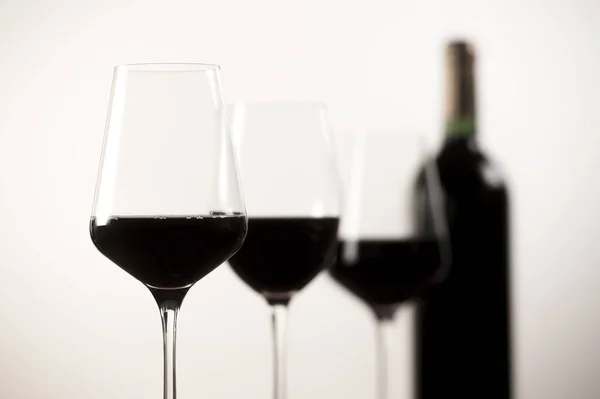 Garrafa de vinho tinto e três copos no fundo branco — Fotografia de Stock
