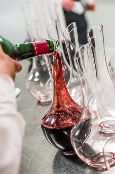 Sommelier at work, pouring wine to decanter while standing near the wine shelf — Stock Photo, Image