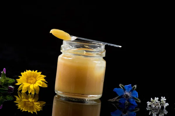 Raw organic royal jelly in bottle with litte spoon on black background