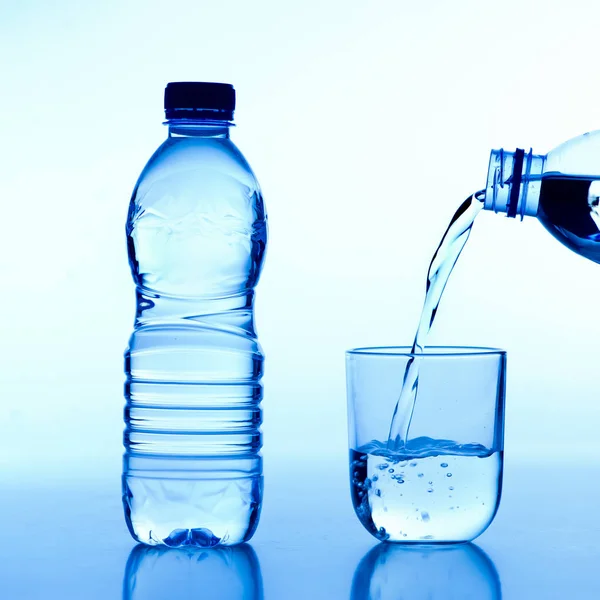 Hand hält Trinkwasserflasche, die Wasser in Glas auf weißem Hintergrund gießt — Stockfoto