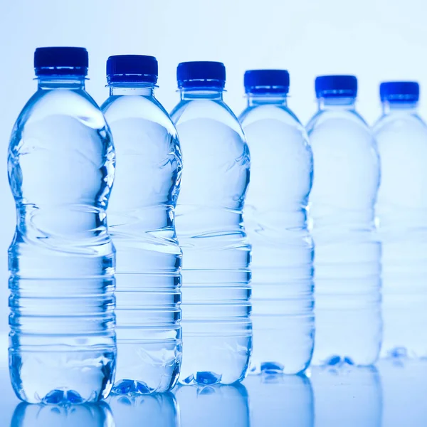 Plastikflaschen mit Wasser isoliert auf blauem Hintergrund — Stockfoto