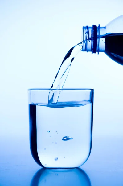 青い背景があるにグラスにボトルから水を注ぐ — ストック写真