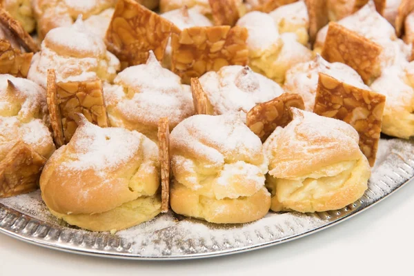 Farces à la crème fourrées à la crème à la vanille et saupoudrées de glaçage sur un plat et de nougatine — Photo