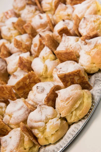 Sbuffi di crema ripieni crema pasticcera alla vaniglia e spolverato con glassa su un piatto e nougatine — Foto Stock