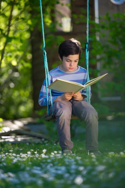 Bambino che legge un libro seduto su un'altalena — Foto Stock