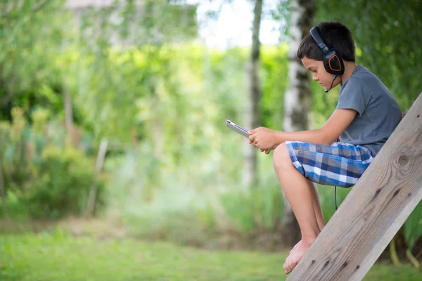 Criança jogando no computador com fones de ouvido ao ar livre — Fotografia de Stock