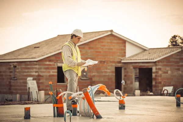 住宅建設現場の背景で保護ヘルメットと設計図の紙とプロのエンジニア建築家の労働者 — ストック写真