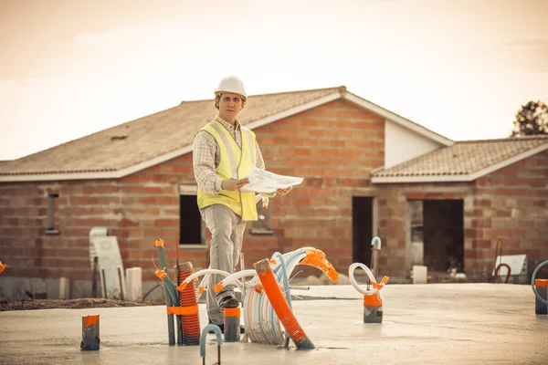 Ingeniero profesional arquitecto trabajador con casco protector y planos de papel en el edificio de la casa de la construcción de fondo —  Fotos de Stock