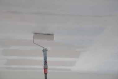 Beyaz duvarları boyayan bir paten, beyaz boyalı tavan.