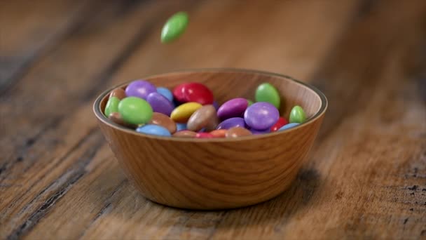Cámara lenta, caramelos coloridos en una caja de cuenco de madera aislada sobre fondo de madera — Vídeos de Stock