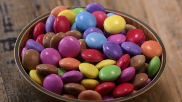 Bonbons colorés dans un bol en bois isolé sur fond de bois — Video