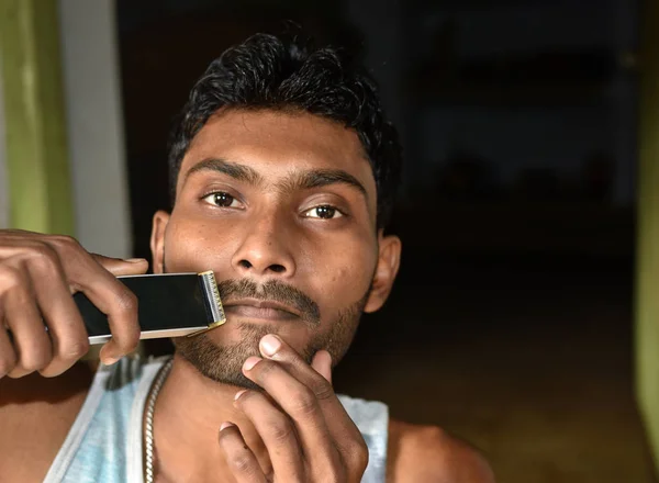 Lähikuva nuoresta miehestä, joka leikkaa partaansa sähköisellä trimmerillä . — kuvapankkivalokuva