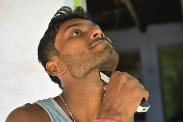Lähikuva nuoresta miehestä, joka leikkaa partaansa sähköisellä trimmerillä — kuvapankkivalokuva