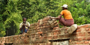 Jhargram, Hindistan - Kasım: Hintli adam çekiçle tuğla bir duvar kırıyor, evini inşa ediyor ve onarıyor.