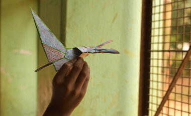 Baskılı kağıttan yapılmış kağıt bir uçağı fırlatmak üzere olan bir çocuğun eli. Pencereden uçmak ve dış dünyayı kucaklamak..