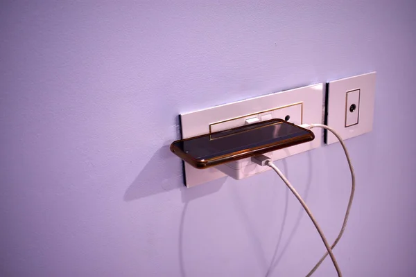 The mobile phone that is charging the battery with the lights in the wall — Stock Photo, Image