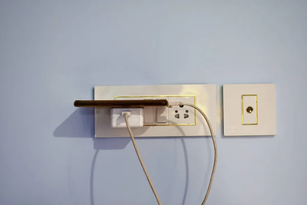 The mobile phone that is charging the battery with the lights in the wall — 스톡 사진