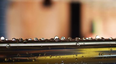 Yağmurlu bir günde metalik bir bardan damlayan kristal yağmur damlaları. Çelik parmaklıkların soyut bir çerçevesi.