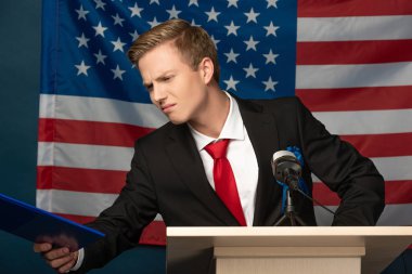 Amerikan bayrağı arka planında Tribünde panoya bakan tatminsiz bir adam.