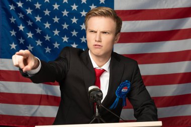 angry man pointing with finger on tribune on american flag background clipart