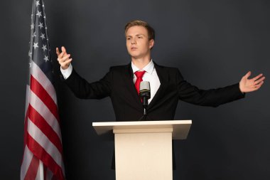 Siyah arka planda Amerikan bayrağı olan duygusal bir adam tribünde konuşuyor.