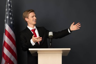 Siyah arka planda Amerikan bayrağı olan tribünde konuşan ve işaret eden duygusal bir adam.