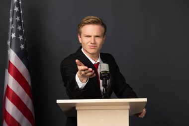 Siyah arka planda Amerikan bayrağı olan Tribünde kamerayı işaret eden duygusal bir adam.