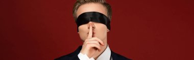 man with blindfold on eyes showing shh gesture on red background clipart