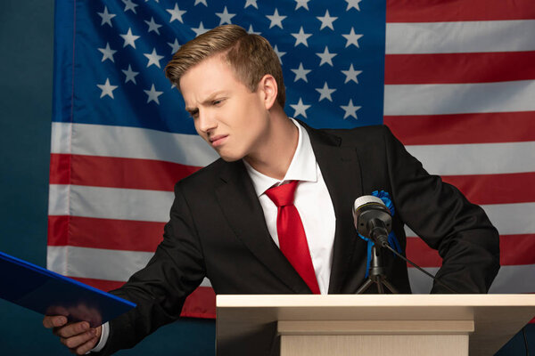 dissatisfied man looking at clipboard on tribune on american flag background