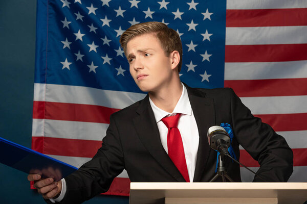 displeased man holding clipboard on tribune on american flag background