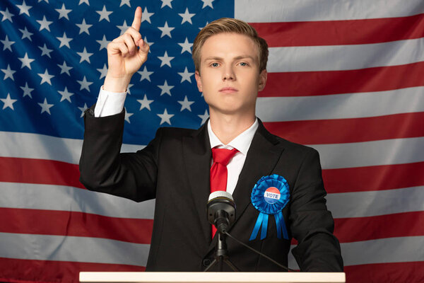 confident man with raised hand on tribune on american flag background