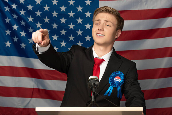 confident man pointing with finger on tribune on american flag background