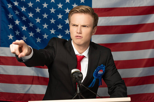 angry man pointing with finger on tribune on american flag background