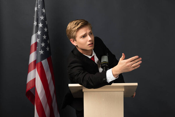 emotional man gesturing on tribune with american flag on black background