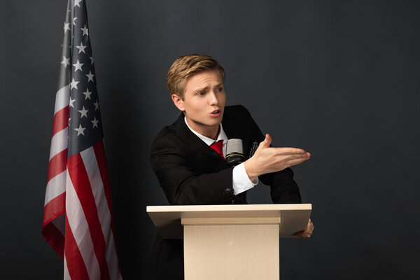 emotional man gesturing on tribune with american flag on black background