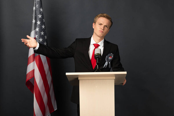 displeased emotional man on tribune with american flag on black background