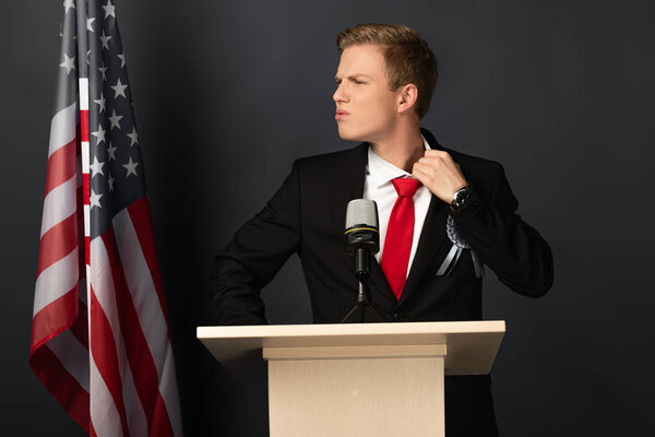 displeased emotional man on tribune with american flag on black background