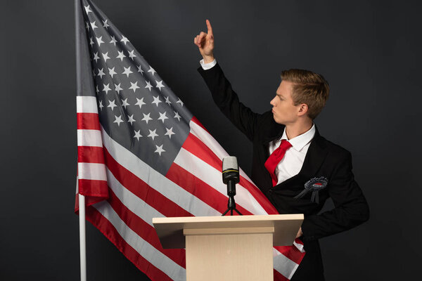 displeased emotional man with raised hand on tribune with american flag on black background