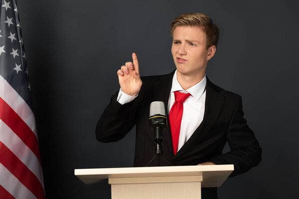 emotional man showing idea gesture on tribune with american flag on black background
