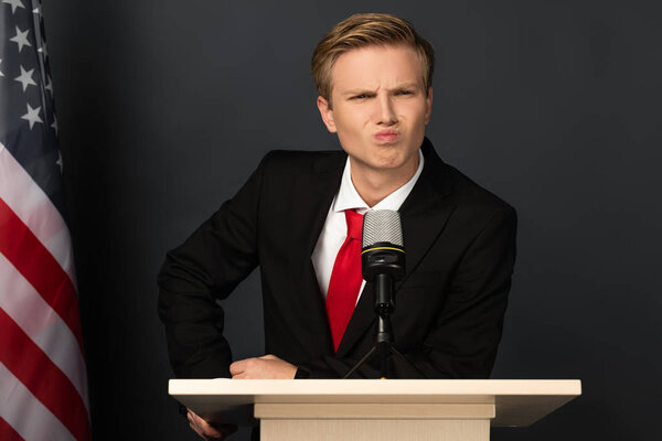 emotional man grimacing on tribune with american flag on black background