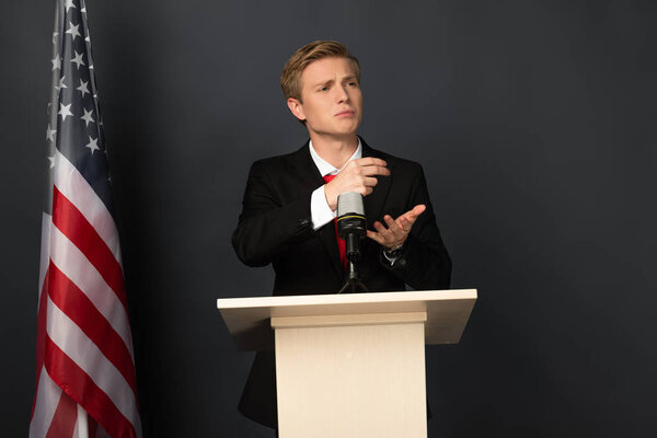 emotional man speaking on tribune with american flag on black background