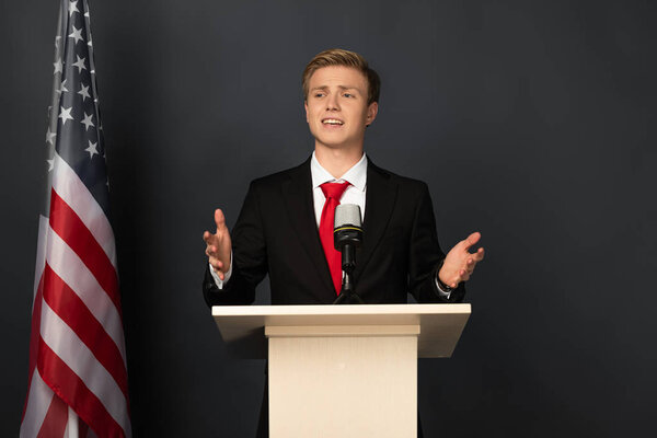 emotional man speaking on tribune with american flag on black background