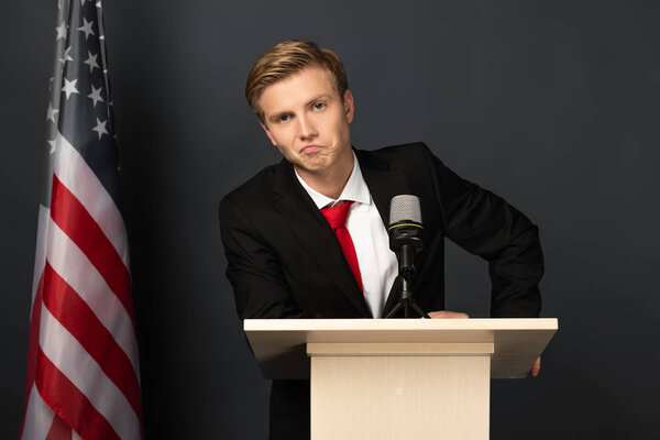 displeased emotional man on tribune with american flag on black background