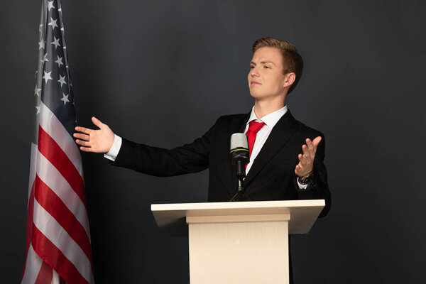 emotional man gesturing on tribune with american flag on black background