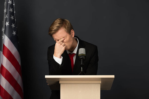 emotional man with obscure face on tribune with american flag on black background
