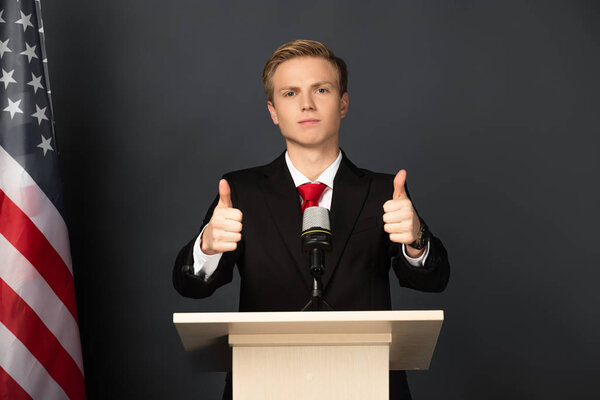  emotional man showing thumbs up on tribune with american flag on black background